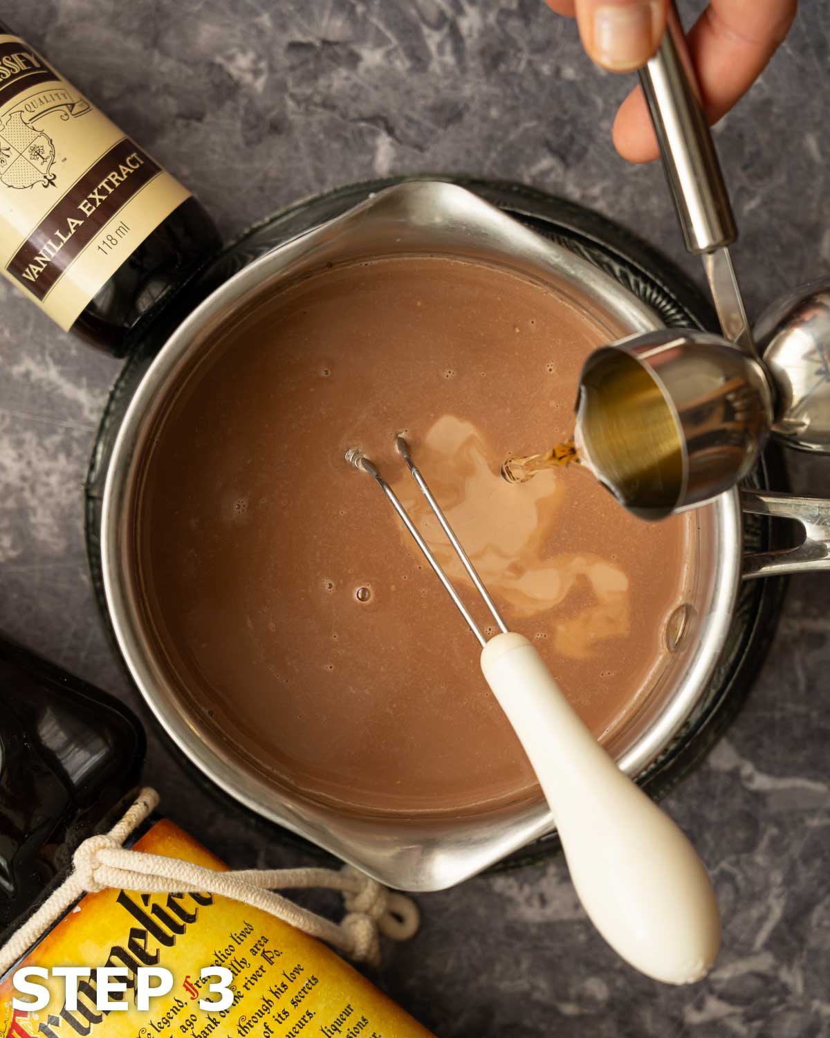 A person pouring hazelnut liqueur into a pan of cream and melted chocolate.