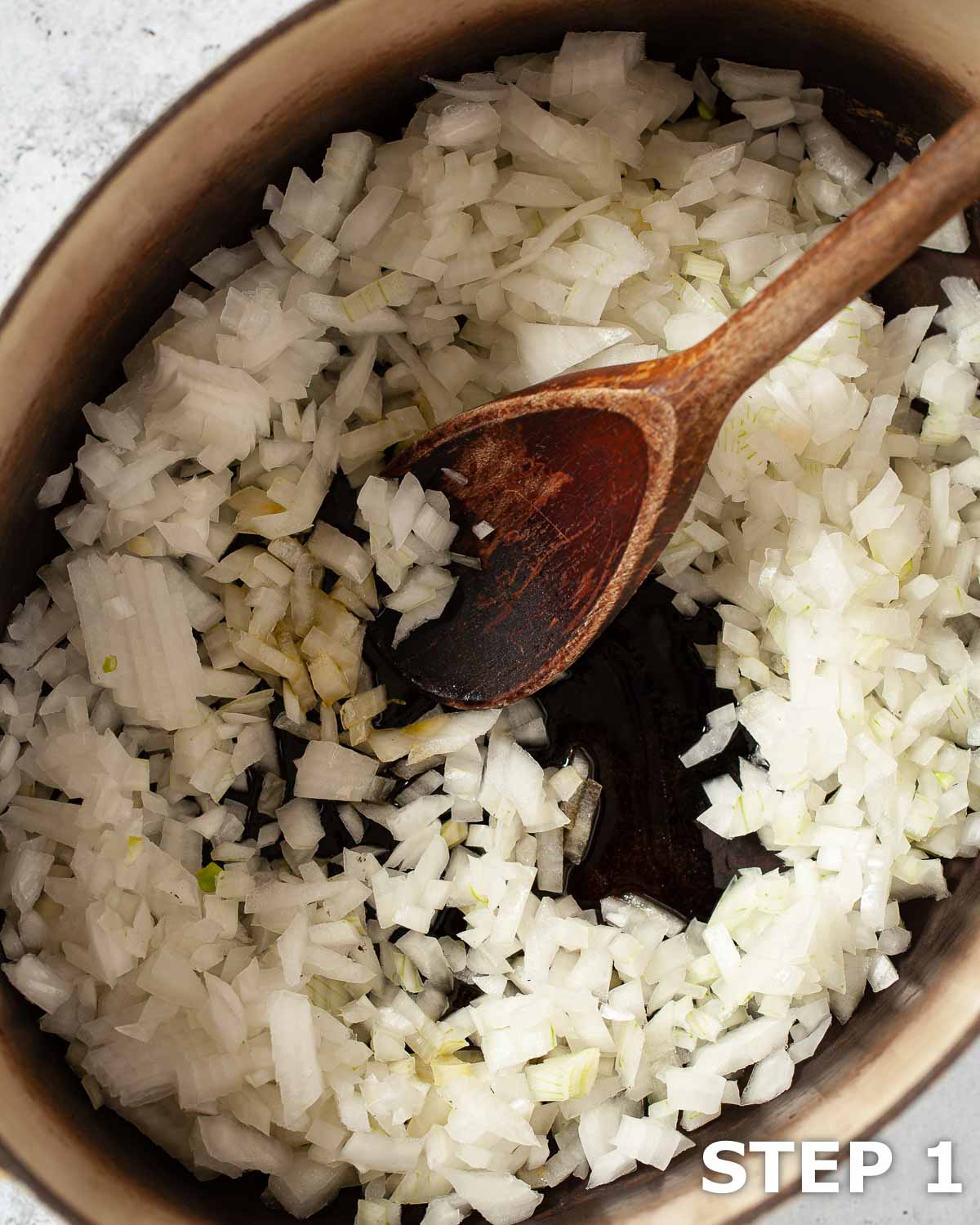 Chopped onions and a wooden spoon in a large pan.