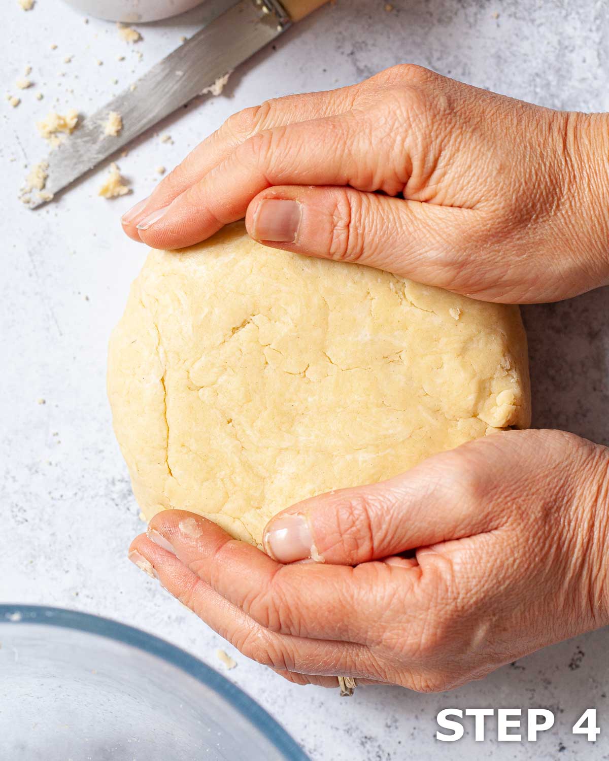 A person shaping shortcrust pastry dough into a disc on a worktop.