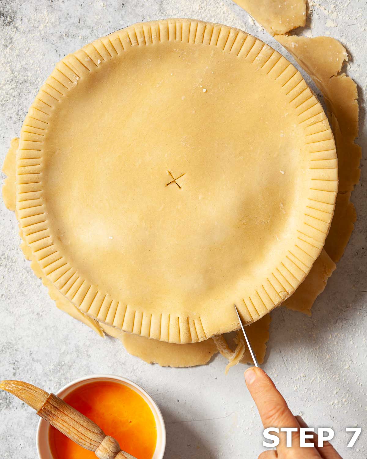 A person cutting a pattern into the edge of a shortcrust pastry pie.