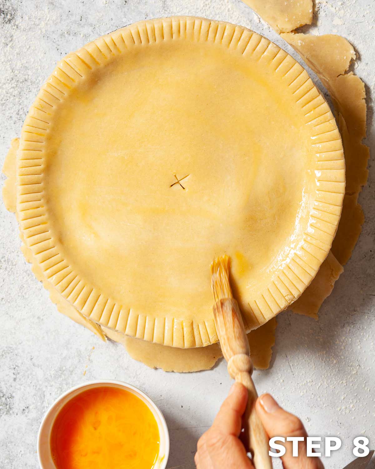 A person brushing the top of a shortcrust pastry pie with beaten egg.