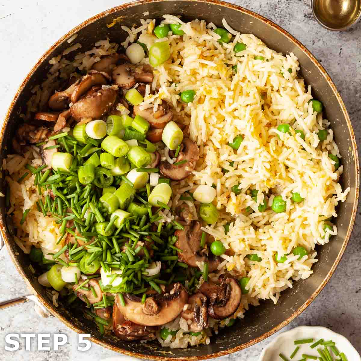 Mushroom, chives, and onion added to a pan of egg fried rice.
