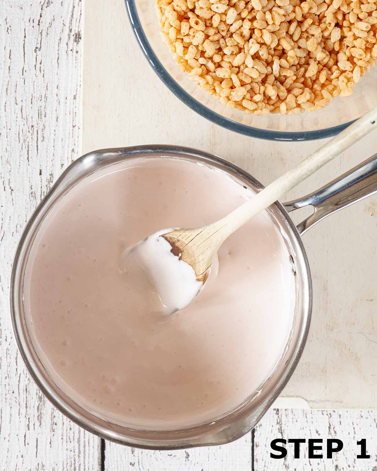 Melted marshmallows in a pan with a bowl of Rice Krispies alongside.