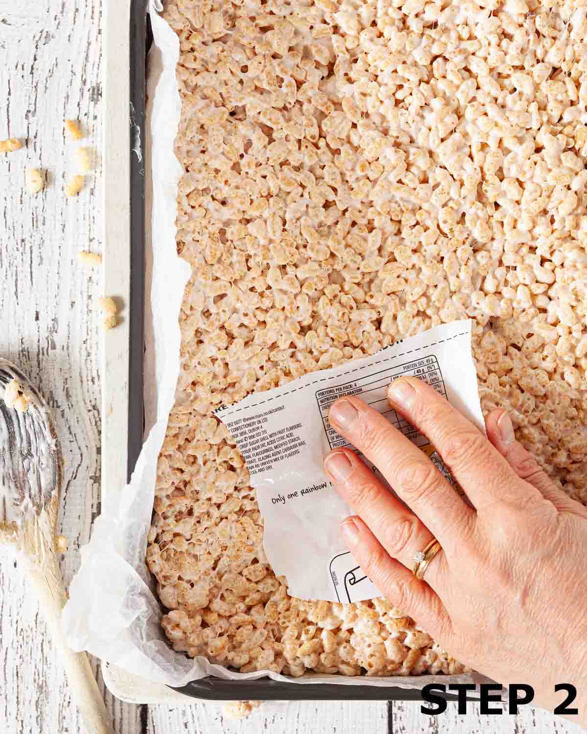 A person pressing Rice Krispie treats mixture into a baking tin.