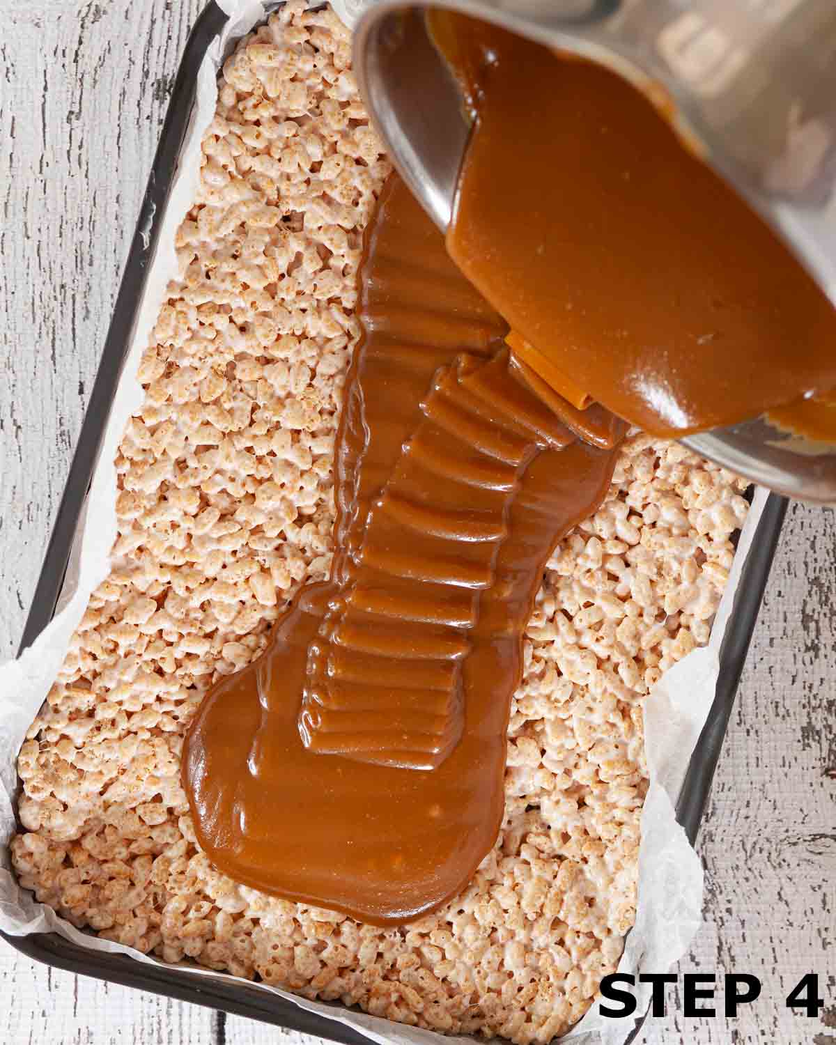 Caramel being poured over a layer of Rice Krispie treats in an oblong tin.