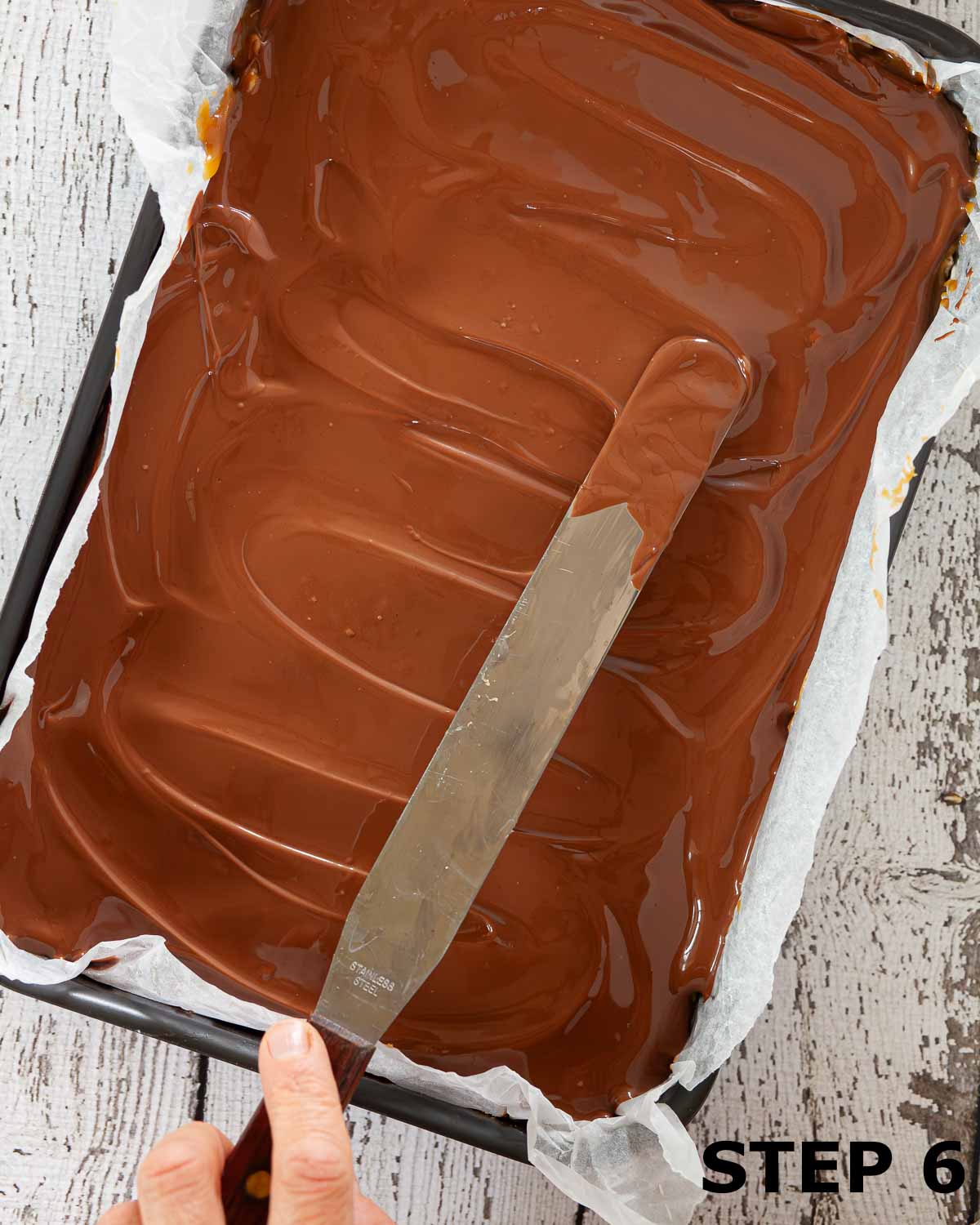 Milk chocolate being spread over a traybake in an oblong tin.