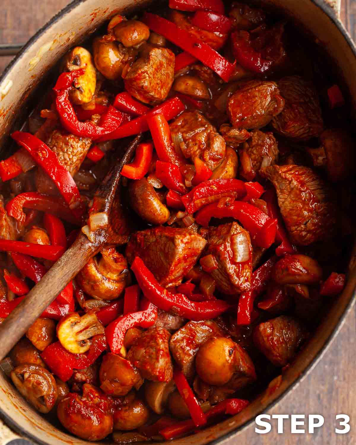 Ingredients for slow cooked goulash in a dutch oven including peppers, mushrooms, beef and onions.