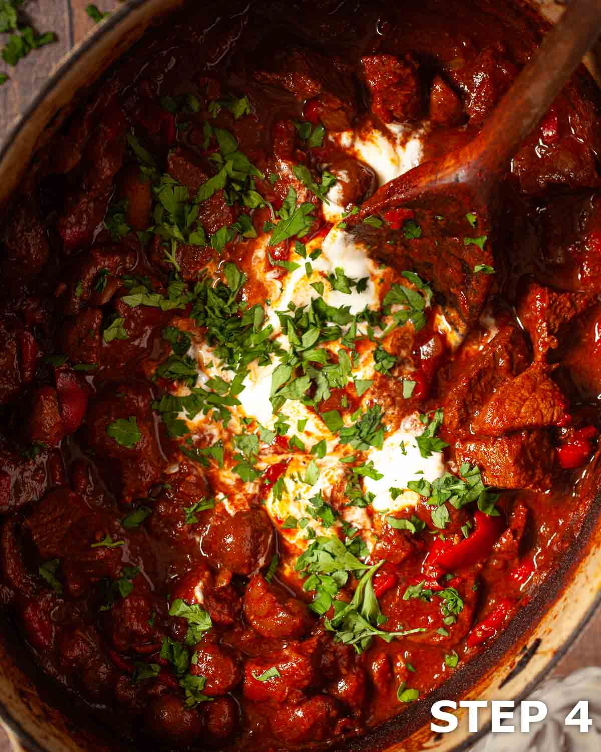Soured cream and chopped parsley being stirred into slow cooked beef goulash.