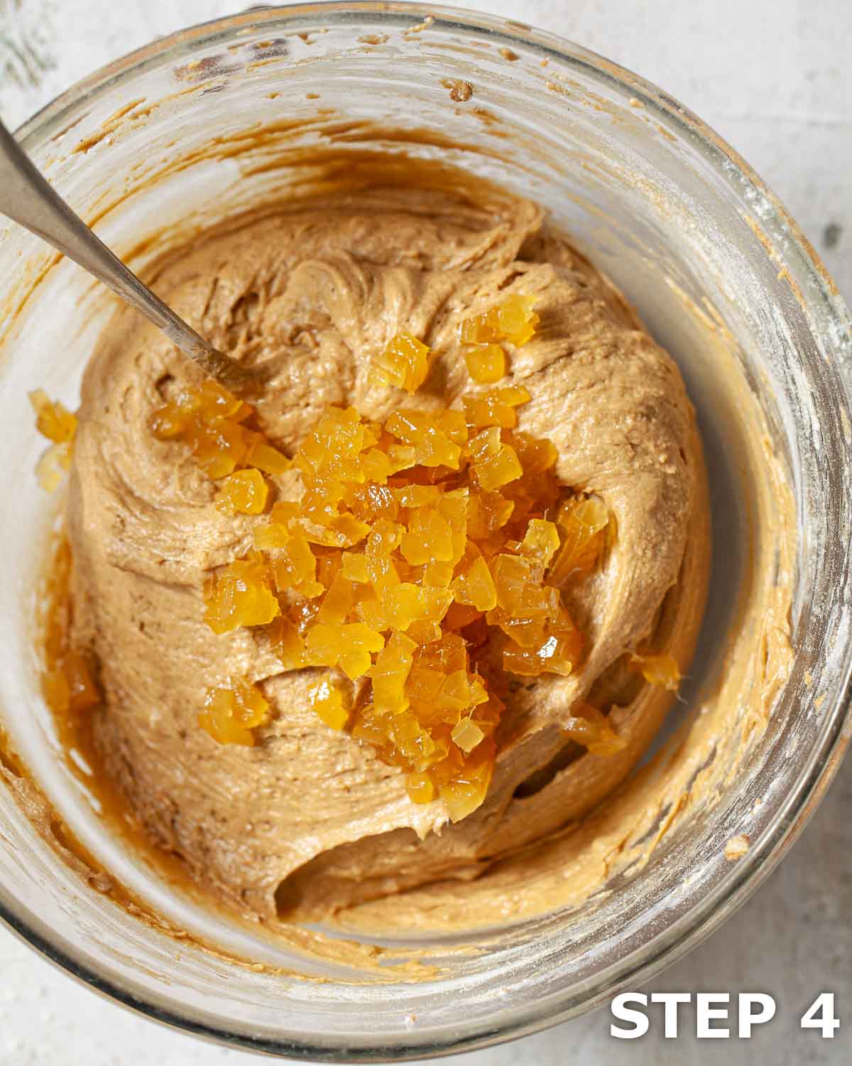 Chopped stem ginger in a bowl of cake batter with a metal spoon.