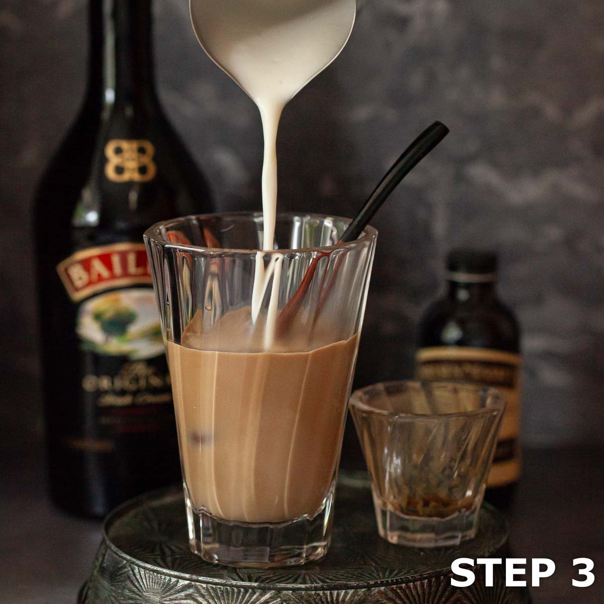 Steamed milk being poured into a heatproof glass with coffeee and Irish cream.
