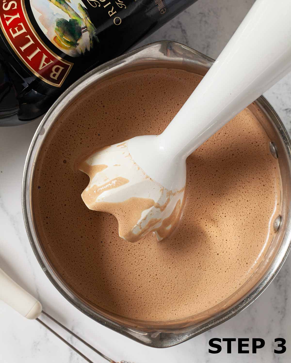 A handheld immersion blender in a pan of Baileys mocha.