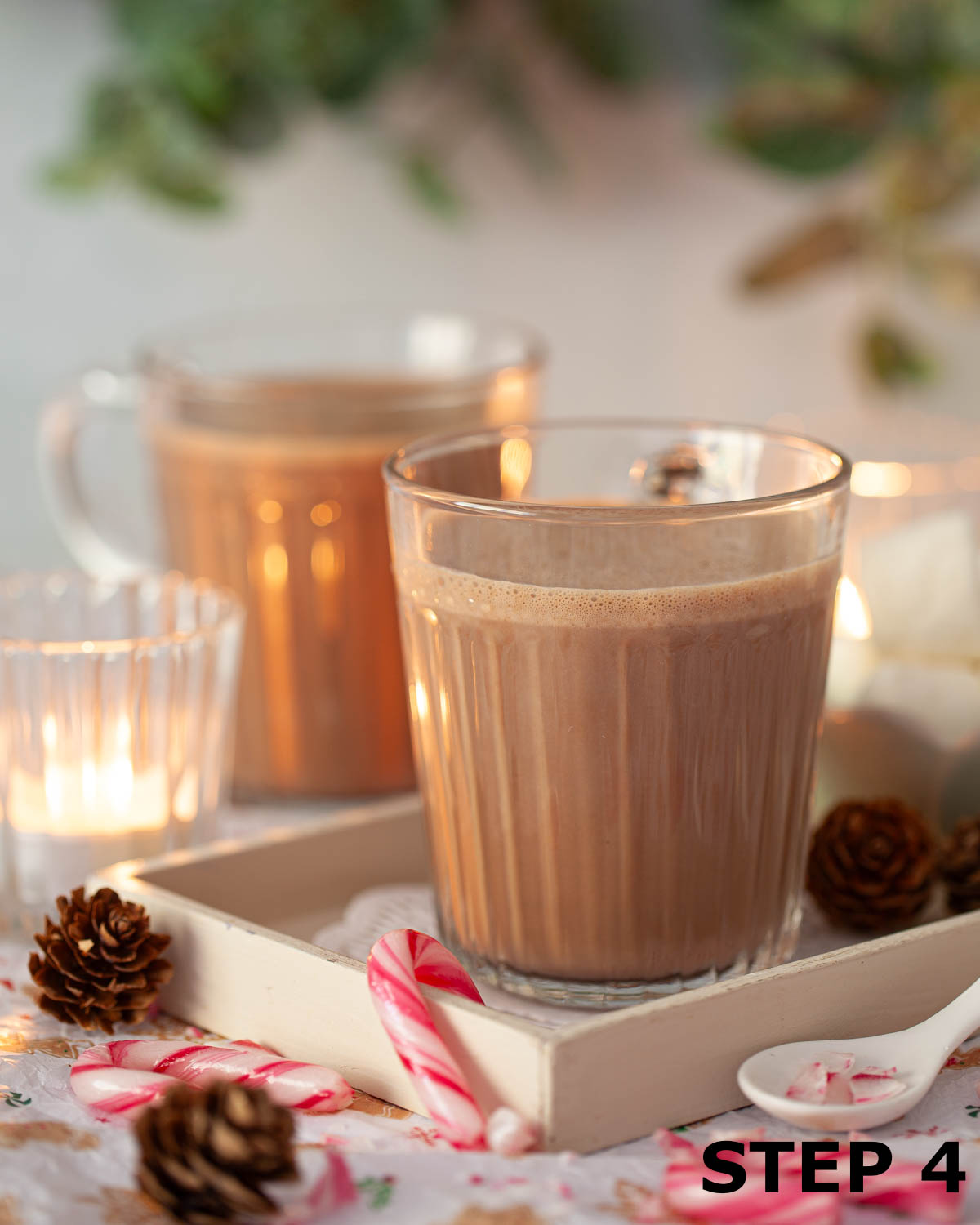 Mugs of hot chocolate with mini candy cane sweets and pine cones alongside.