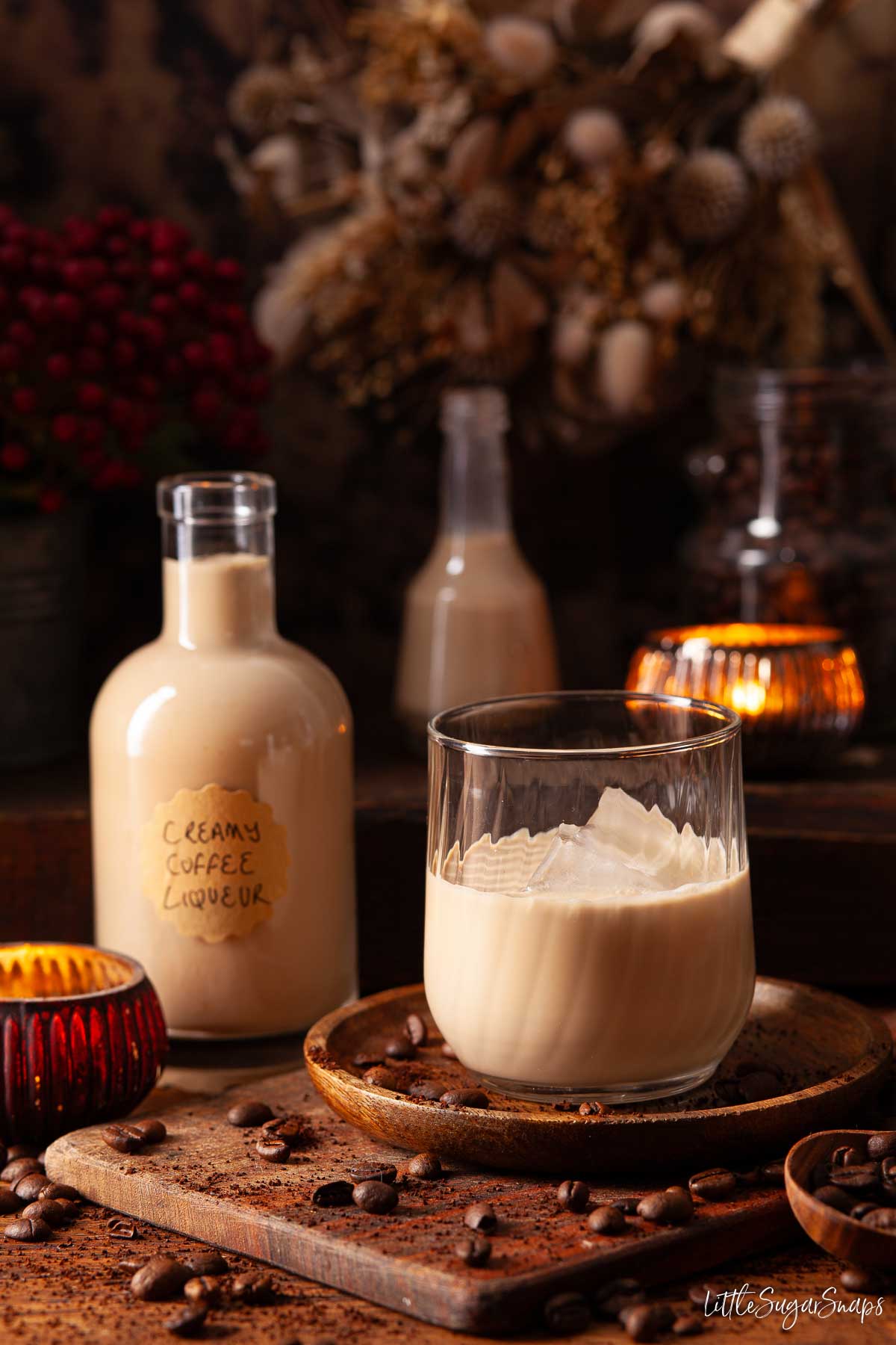 Homemade coffee liqueur in a glass with ice and a full bottle alongside.