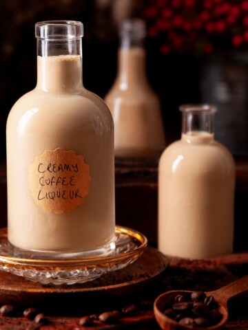 Three bottles of homemade coffee liqueur surrounded by coffee beans.