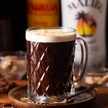A glass of coffee and Malibu rum with cream float and alcohol bottles in the background.