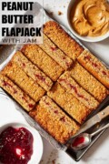 Slices of peanut butter and jam flapjack lined up on a tray with text overlay.