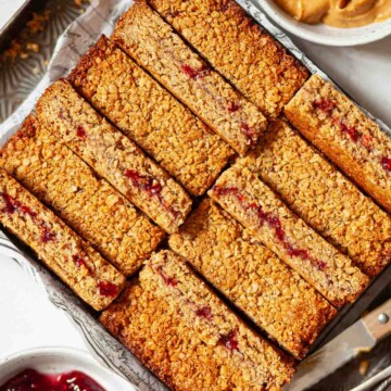 Slices of chewy peanut butter flapjack with a jam centre lined up on a tray.