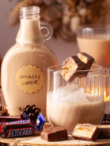 Peanut butter liqueur served over ice with slices of Snickers chocolate on a cocktail pick.