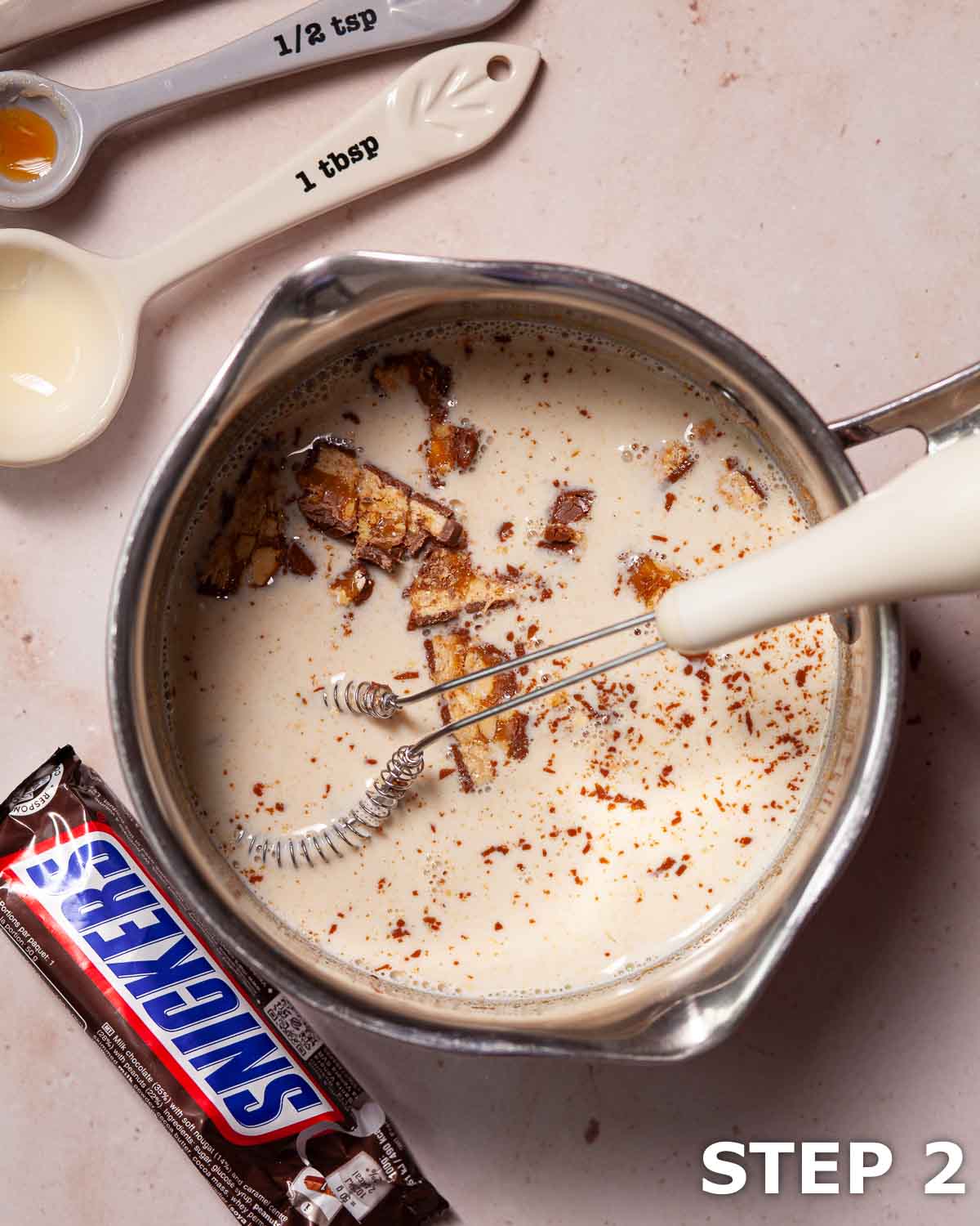 Chopped up Snickers bar in a pan of warm ingredeitns for peanut liqueur.