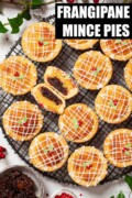 Labelled mince pies with frangipane and icing on top on a wire rack. One pie is cut in half.