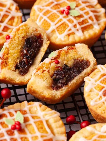A cut open frangipane mince pie surrounded by whole pies on a wire rack.