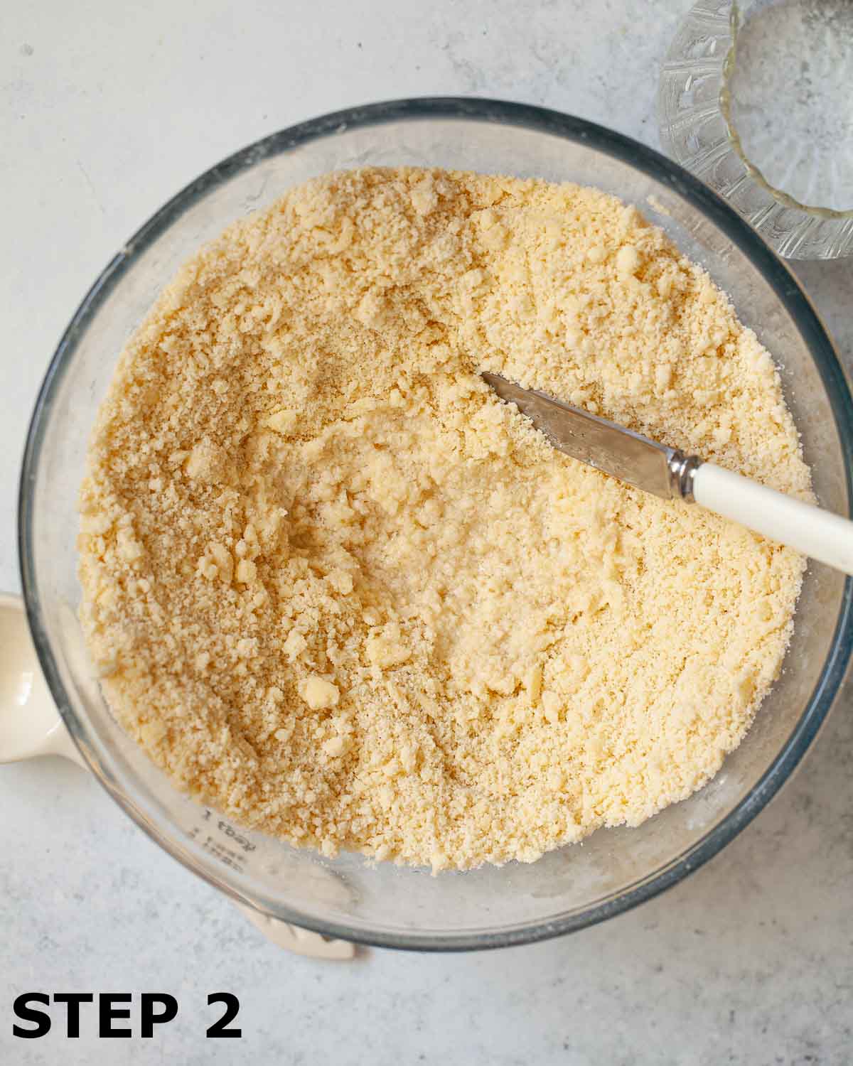 Water about to be stirred into rubbed butter, flour and icing sugar with a blunt knife.