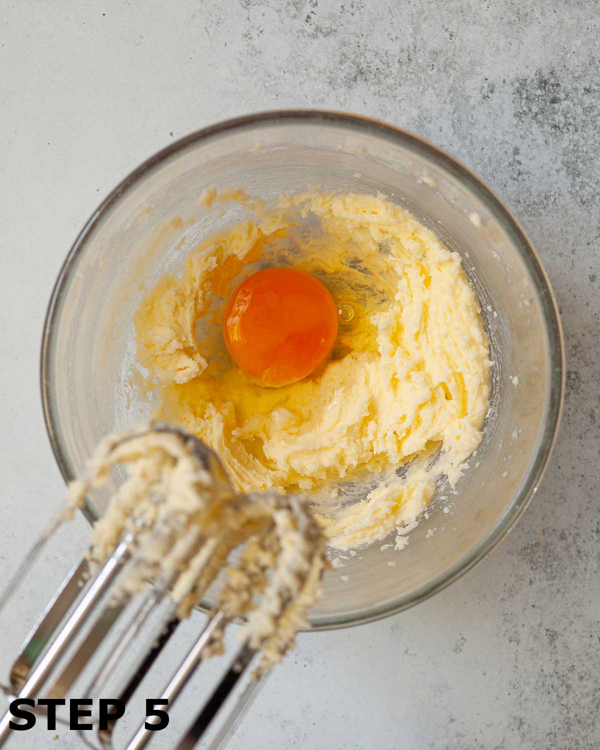 Creamed butter and sugar in a bowl with an egg ready to be mixed in with electric beaters.