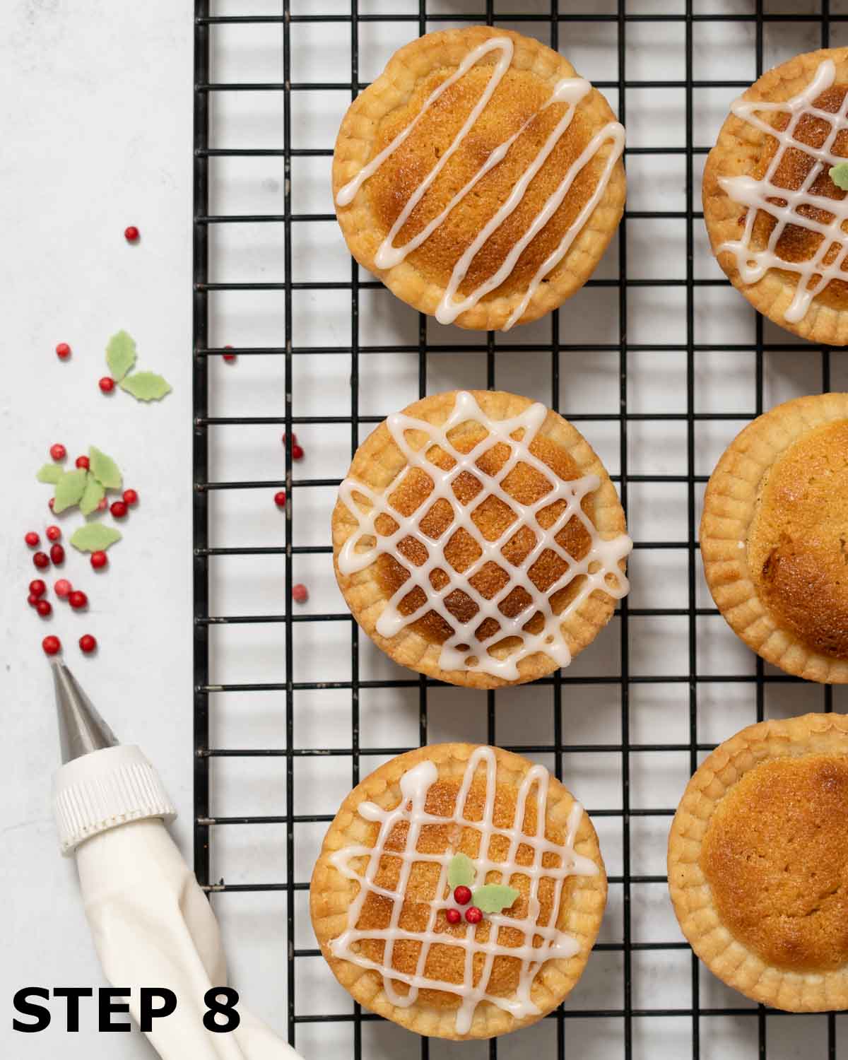Frangipane mince pies being drizzled with white icing and garnished with festive sugar shapes.