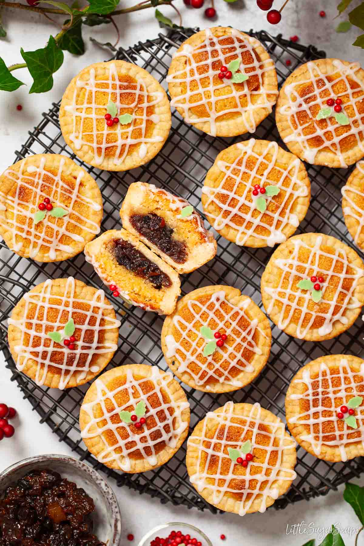 Mince pies with frangipane and icing on top on a wire rack. One pie is cut in half.
