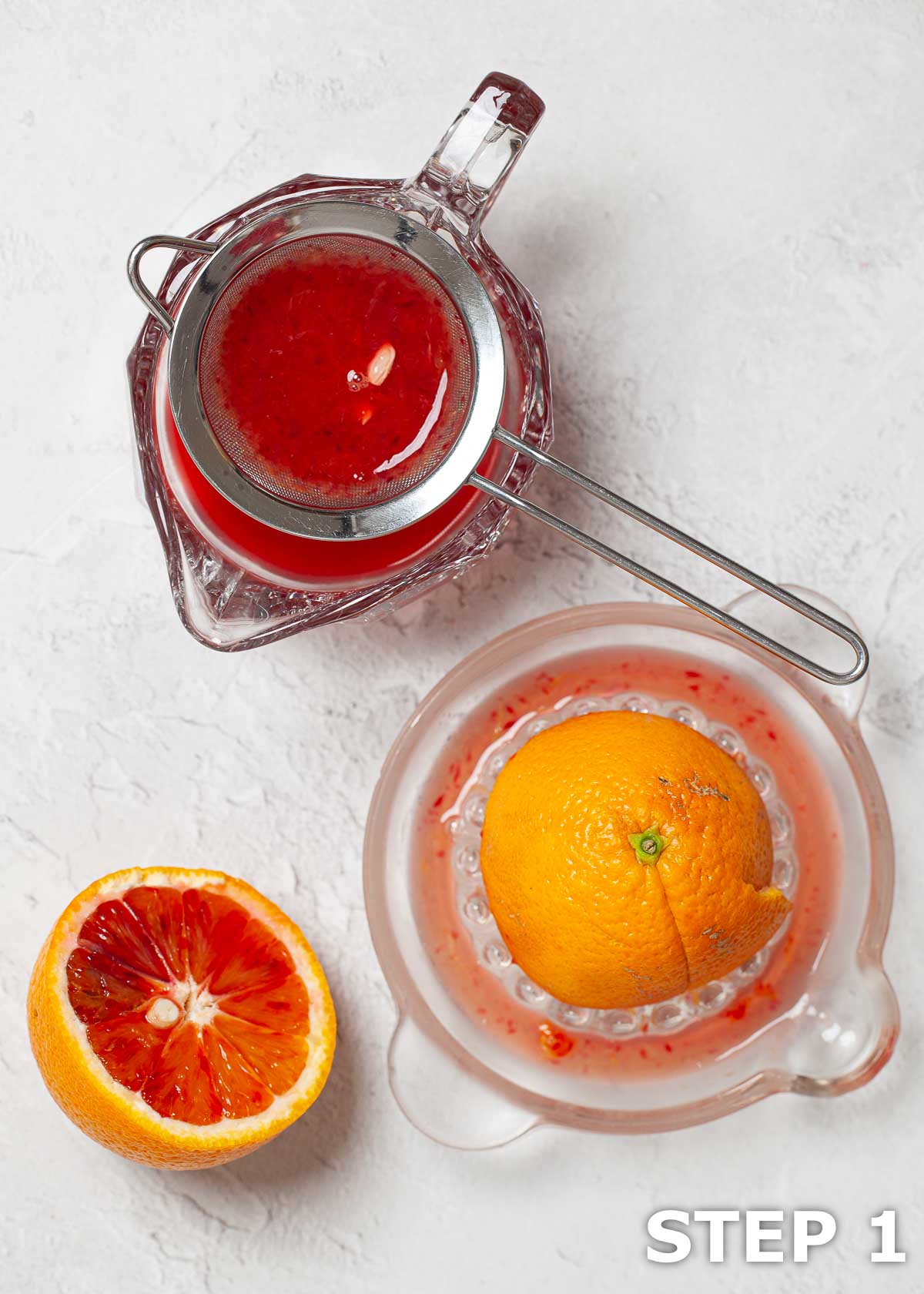 Blood oranges cut, squeezed and the juice being strained through a sieve.