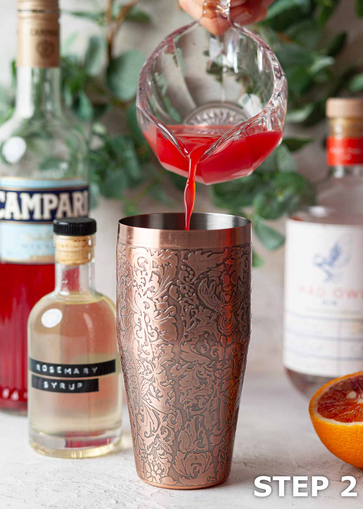 Juice being poured into a cocktail shaker for a blood orange and rosemary syrup cocktail.