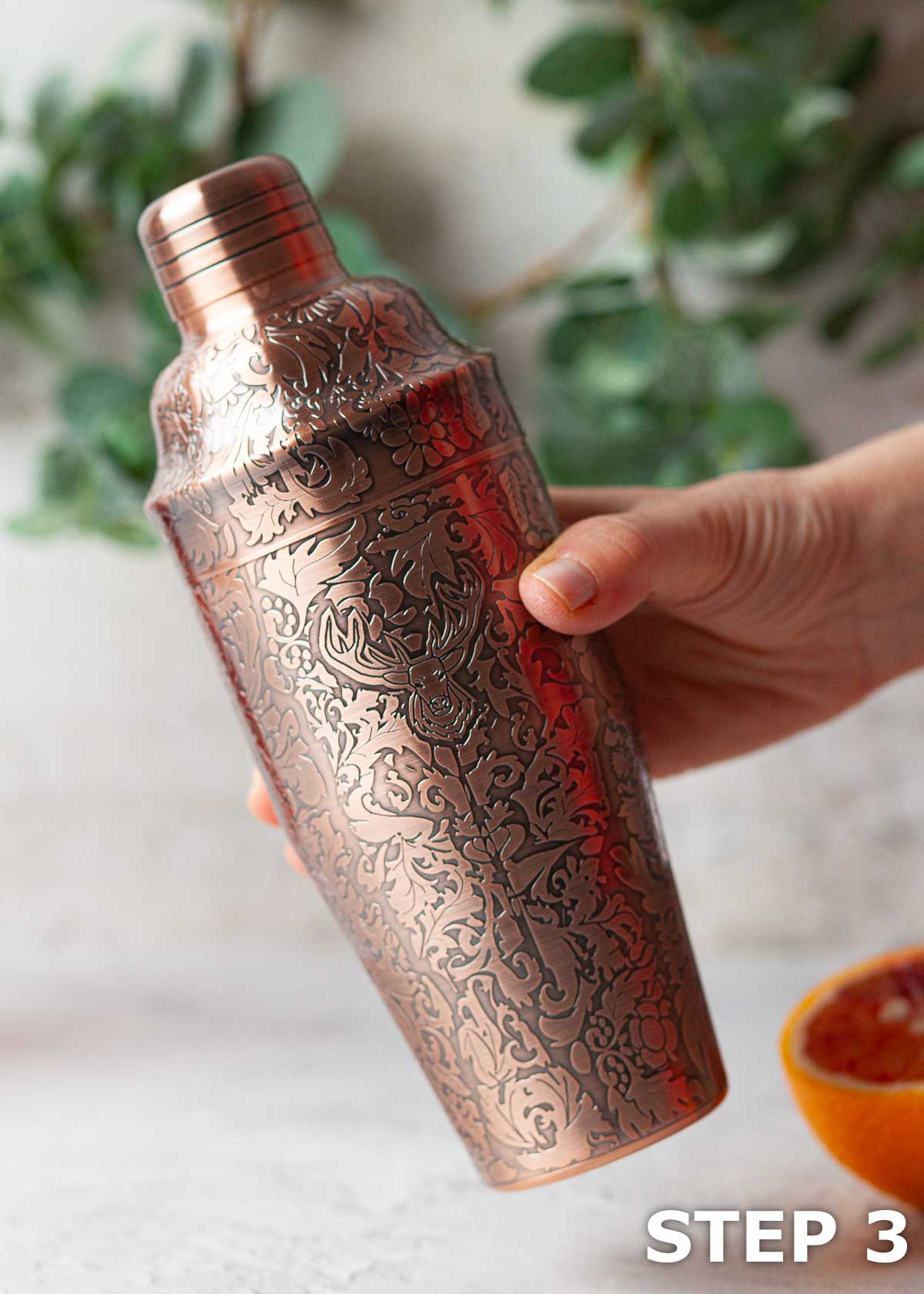 A person holding an embossed copper cocktail shaker.
