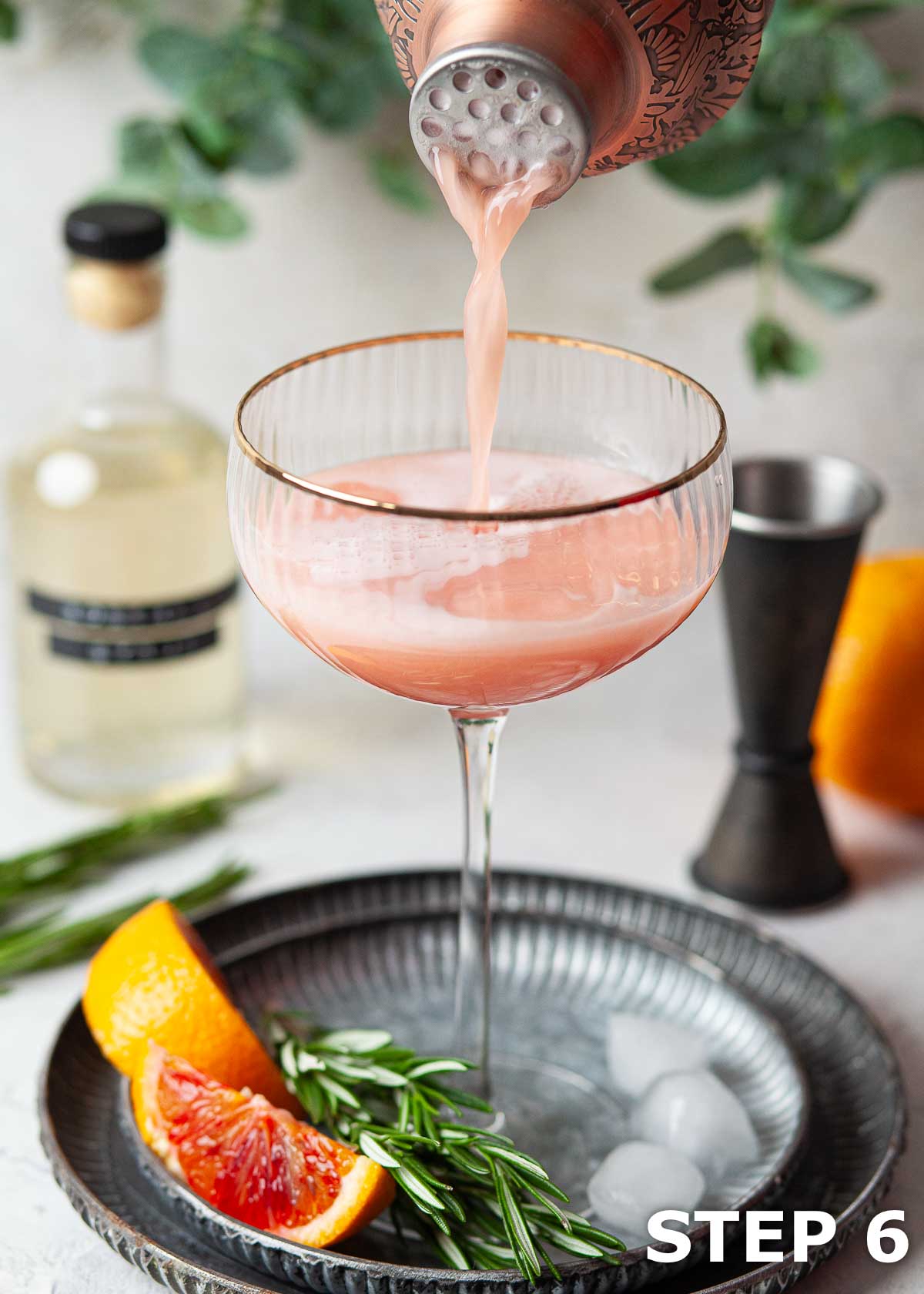 A blood orange martini being poured into a gold-rimmed cocktail glass.