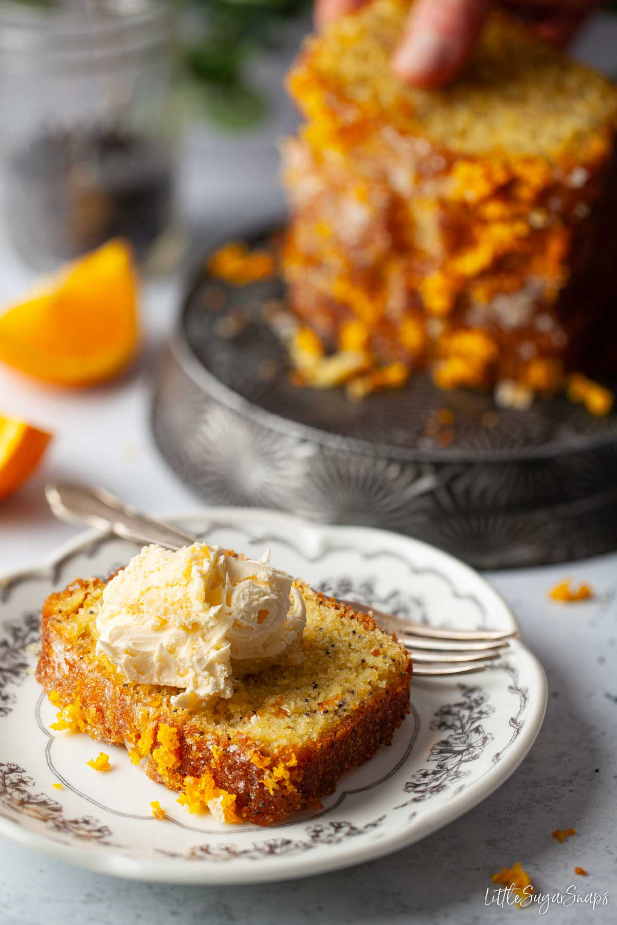 A plated slice of orange and poppy seeds cake topped with clotted cream.