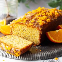 A partially sliced orange and poppy seeds cake on an upturned metal plate.