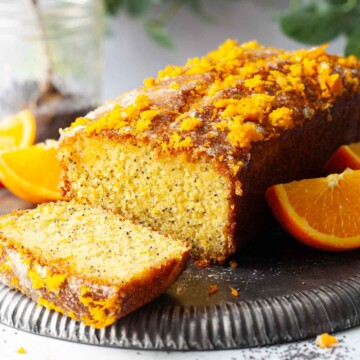 A partially sliced orange and poppy seeds cake on an upturned metal plate.