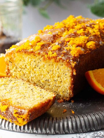 A partially sliced orange and poppy seeds cake on an upturned metal plate.