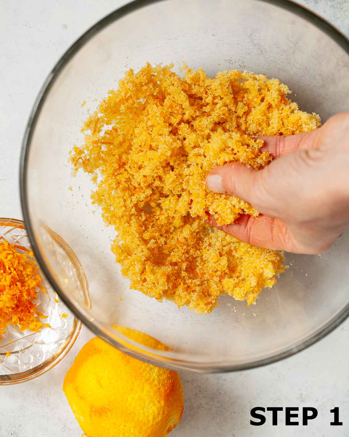 A person rubbing orange zest into caster sugar in a bowl.