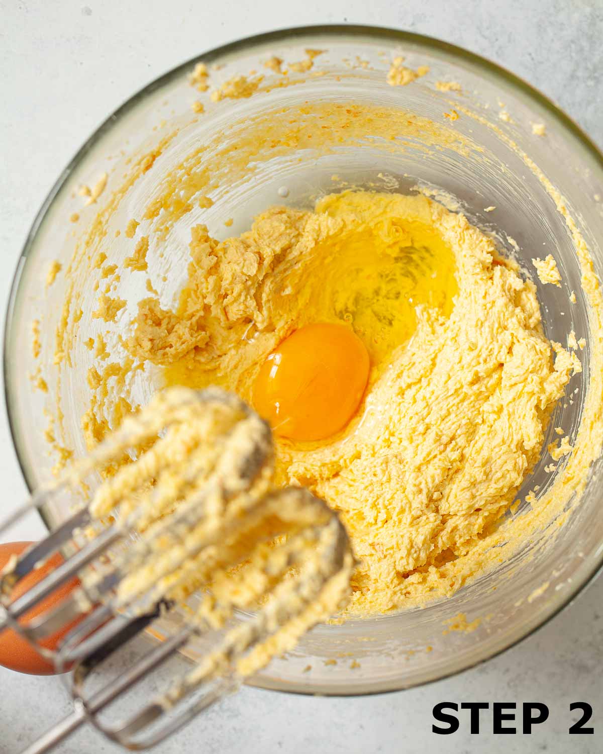 An egg about to be mixed into creamed butter and sugar using electric beaters.