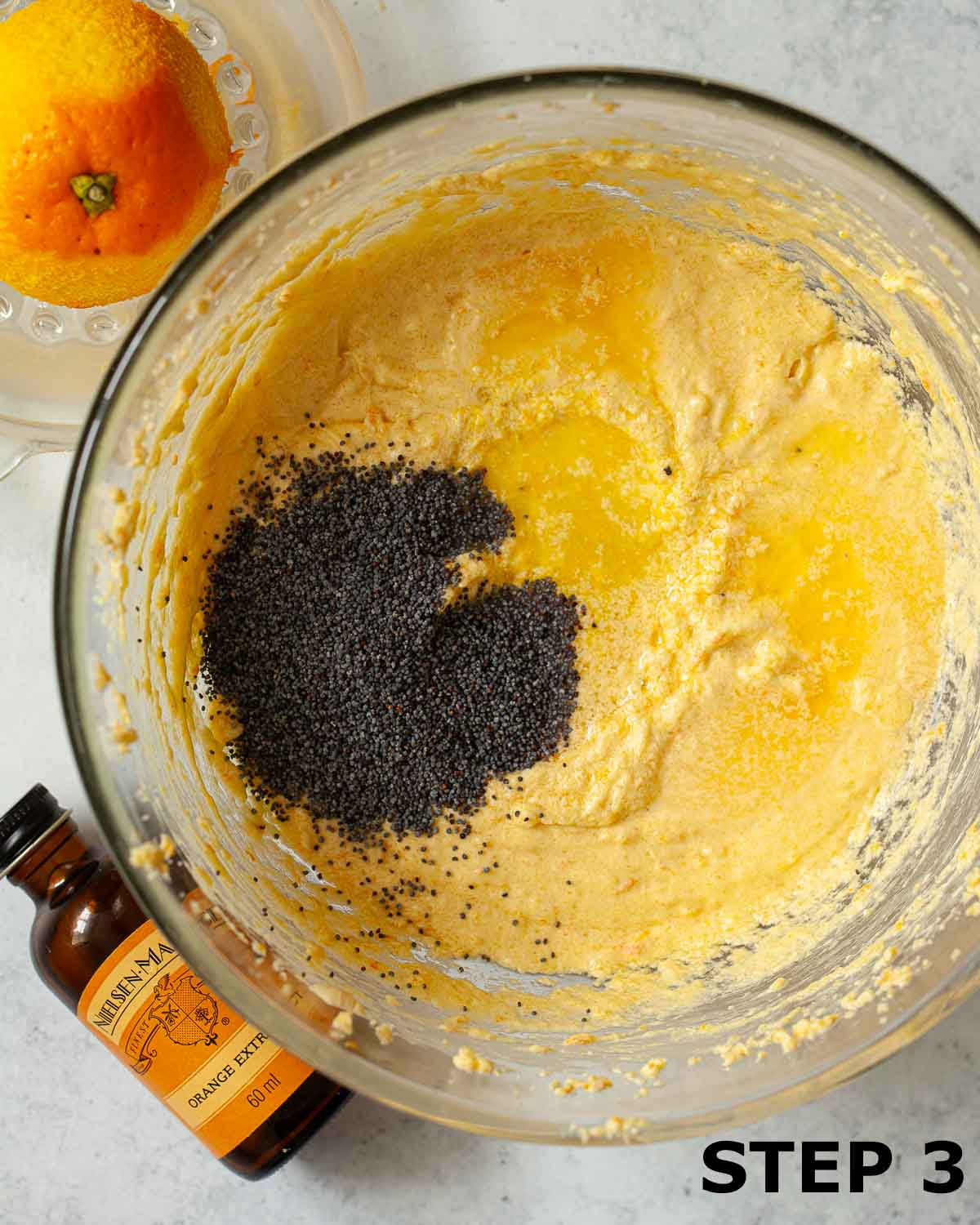 Poppy seeds, orange extract and orange juice in a bowl of cake batter.