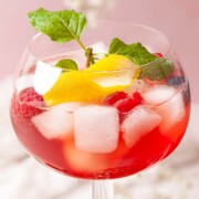 Pomegranate cocktail in a copa glass with lemon, mint and berry garnish.