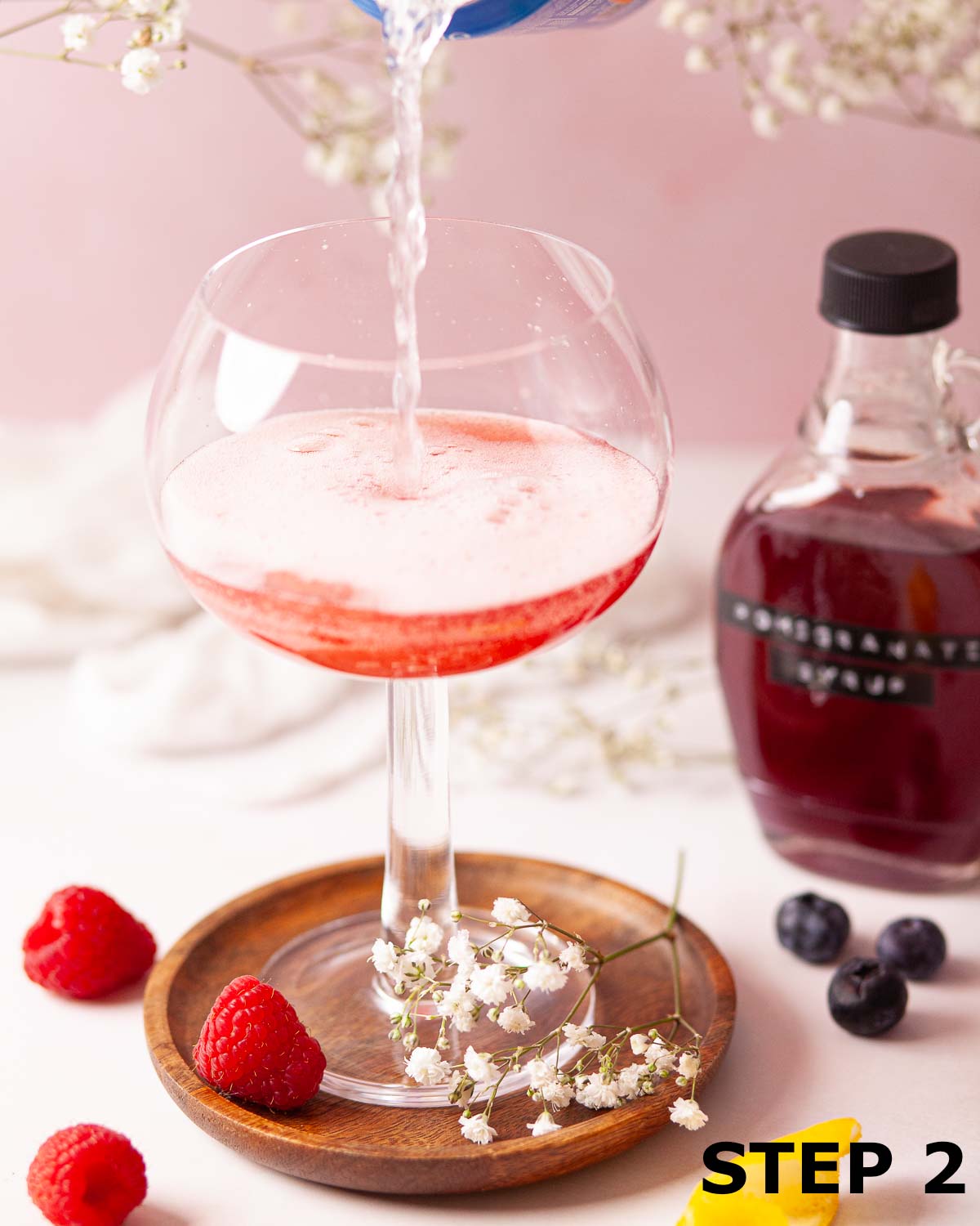 Lemonade being poured over grenadine syrup in a copa glass.