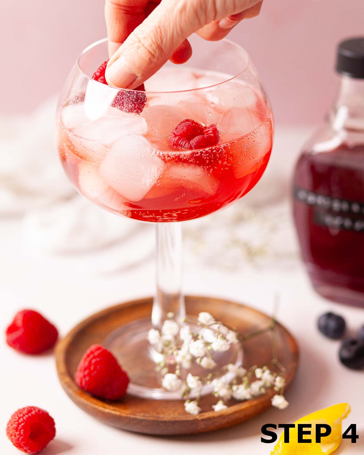 A person adding fresh raspberries to a pomegranate mocktail.
