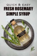 A labelled bottle of homemade rosemary syrup on a metal plate with fresh rosemary sprigs