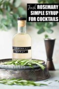 Labelled rosemary simple syrup for cocktails with a jigger in the background and fresh rosemary on a plate.