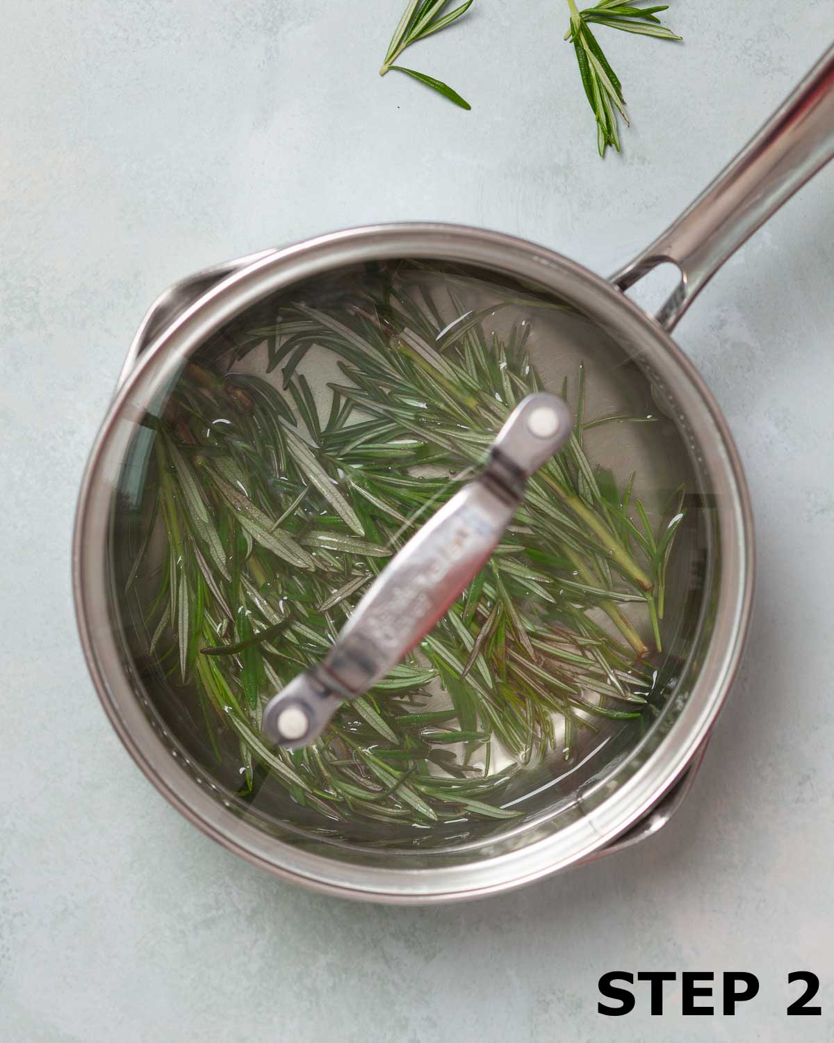 A saucepan containing simple syrup that is infusing in fresh rosemary.
