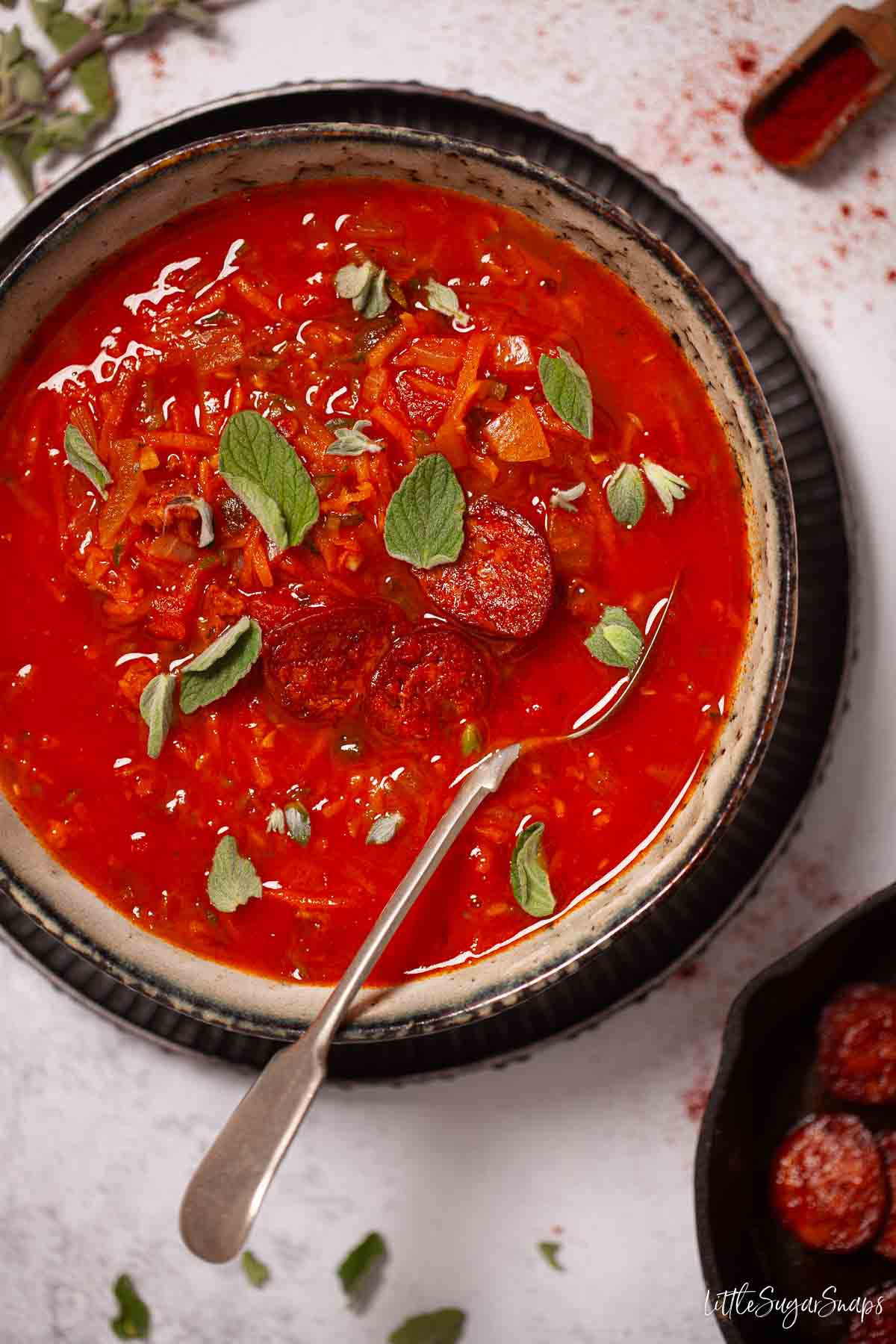 A bowl of carrot and tomato soup garnished with fried chorizo and fresh oregano.