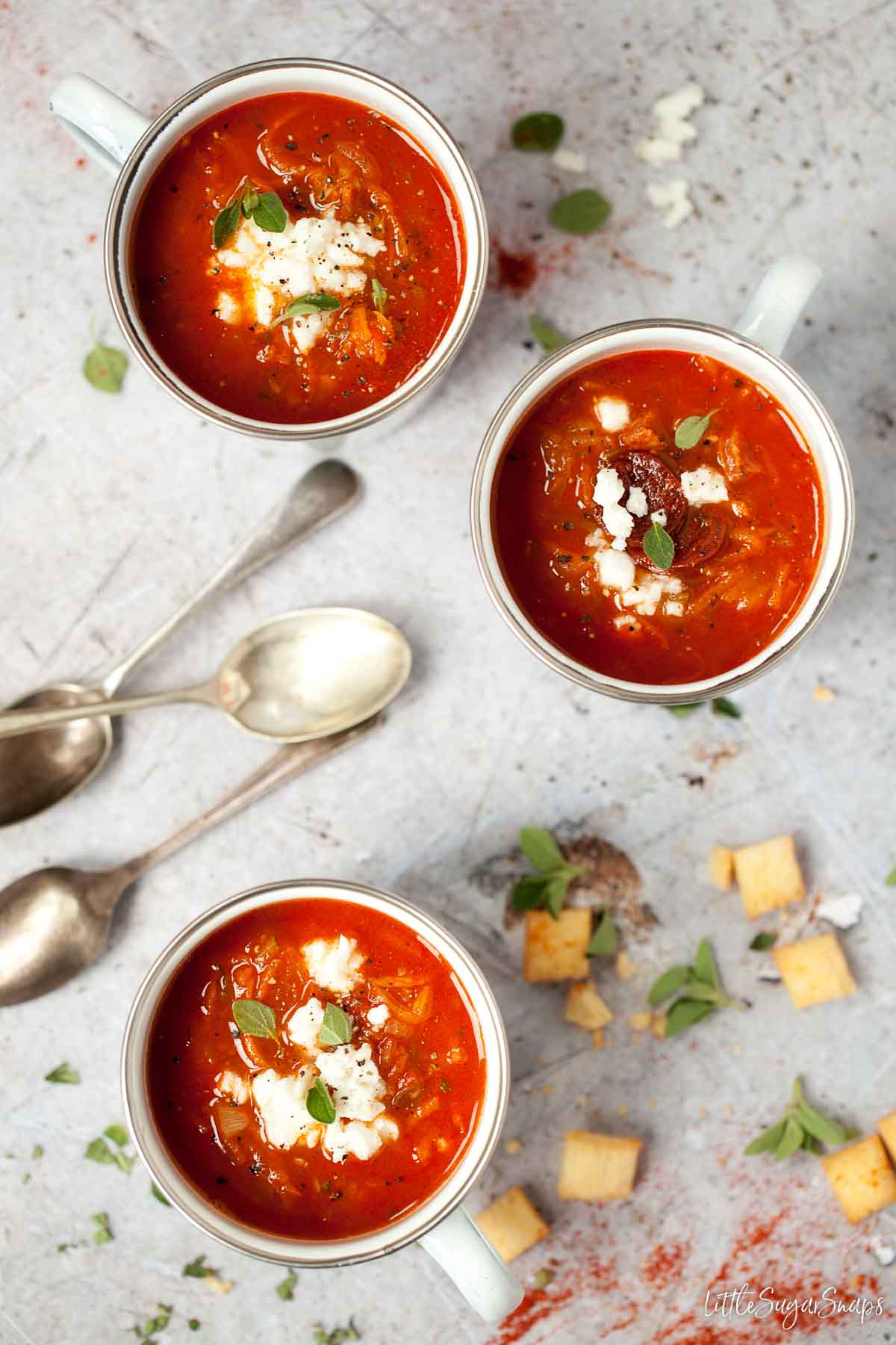 Mugs of tomato, carrot and courgette soup topped with chorizo, feta and oregano.