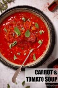 A bowl of carrot and tomato soup garnished with fried chorizo and fresh oregano with text overlay.