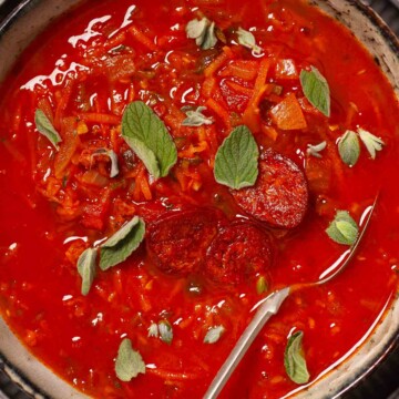 A bowl of carrot and tomato soup garnished with fried chorizo and fresh oregano.
